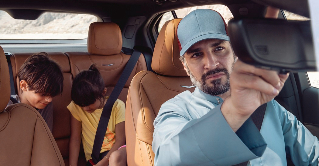 man looks in rearview mirror at children in back seat fastening their seat belts